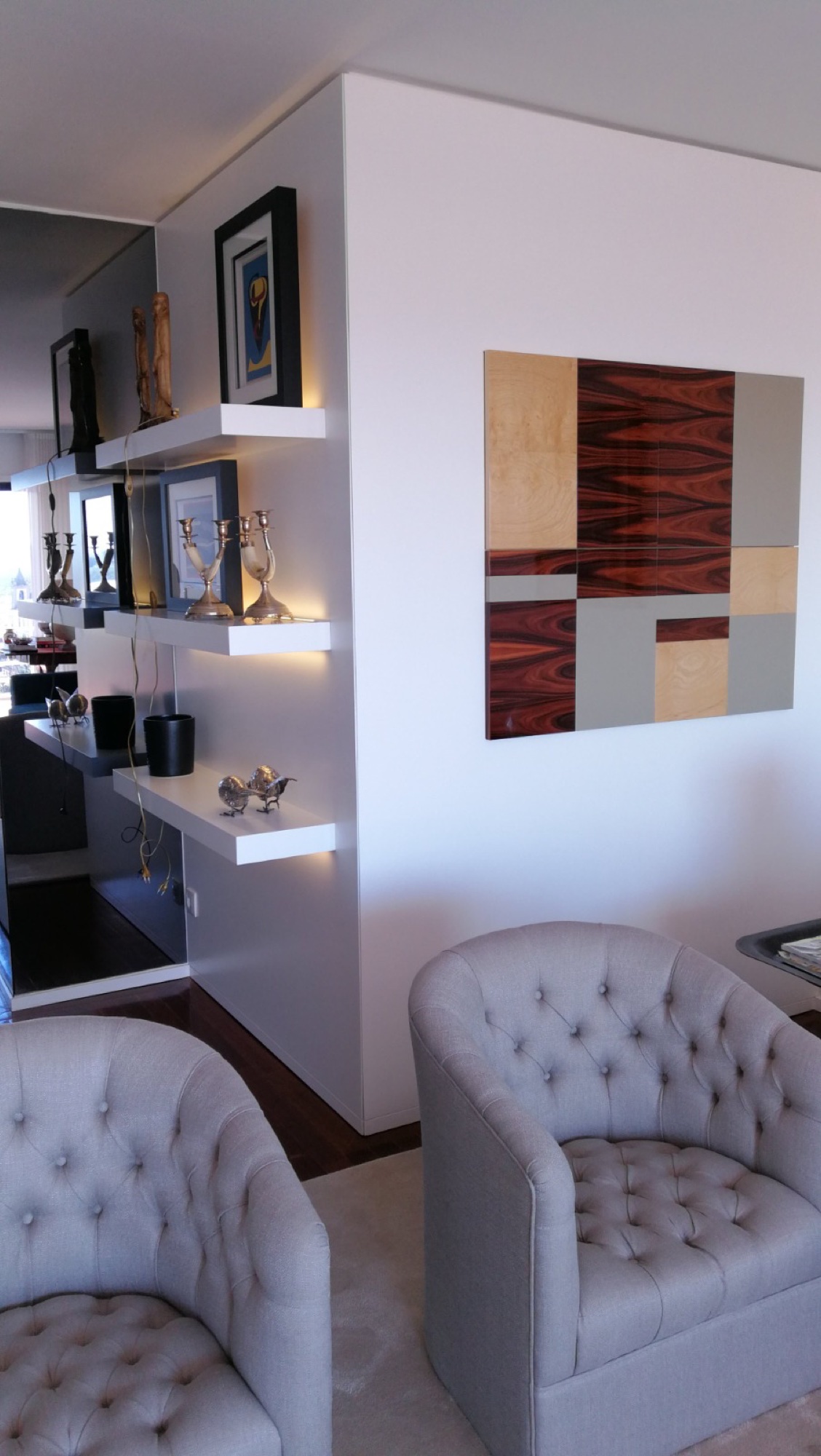 Sala com poltronas cinza e prateleiras brancas