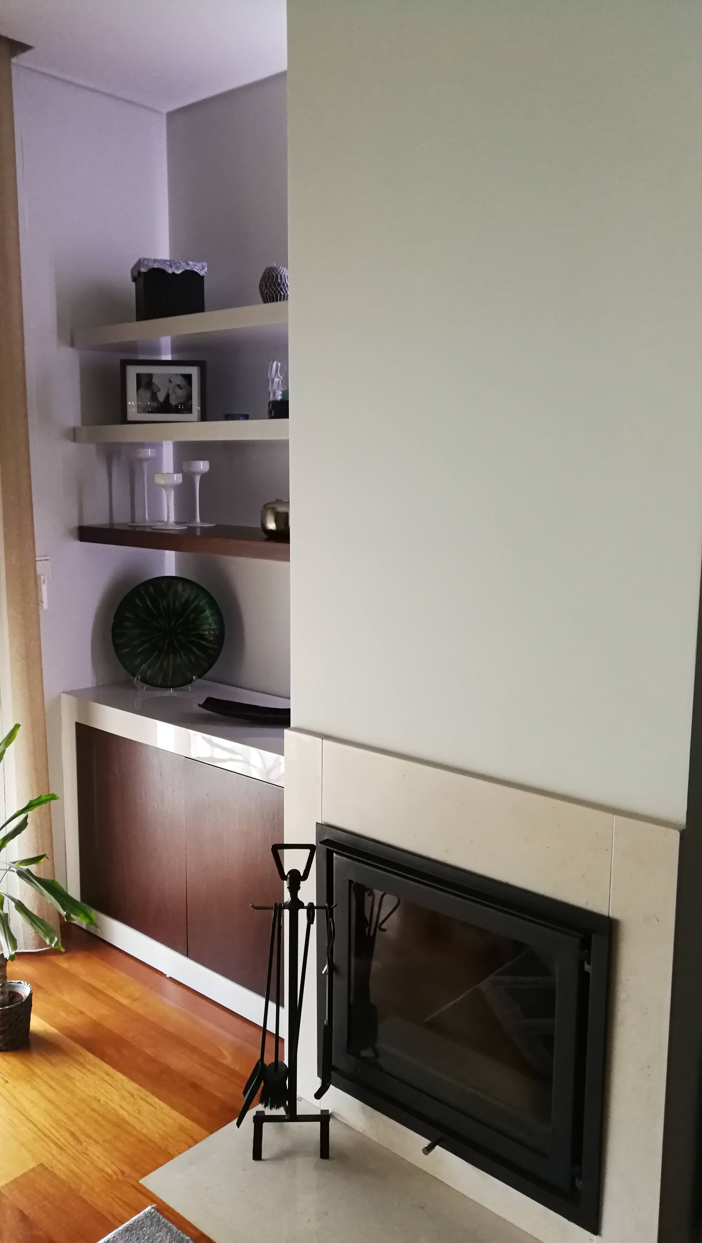 Sala com lareira de recuperador embutida em parede de pedra, estantes flutuantes e armario em madeira escura