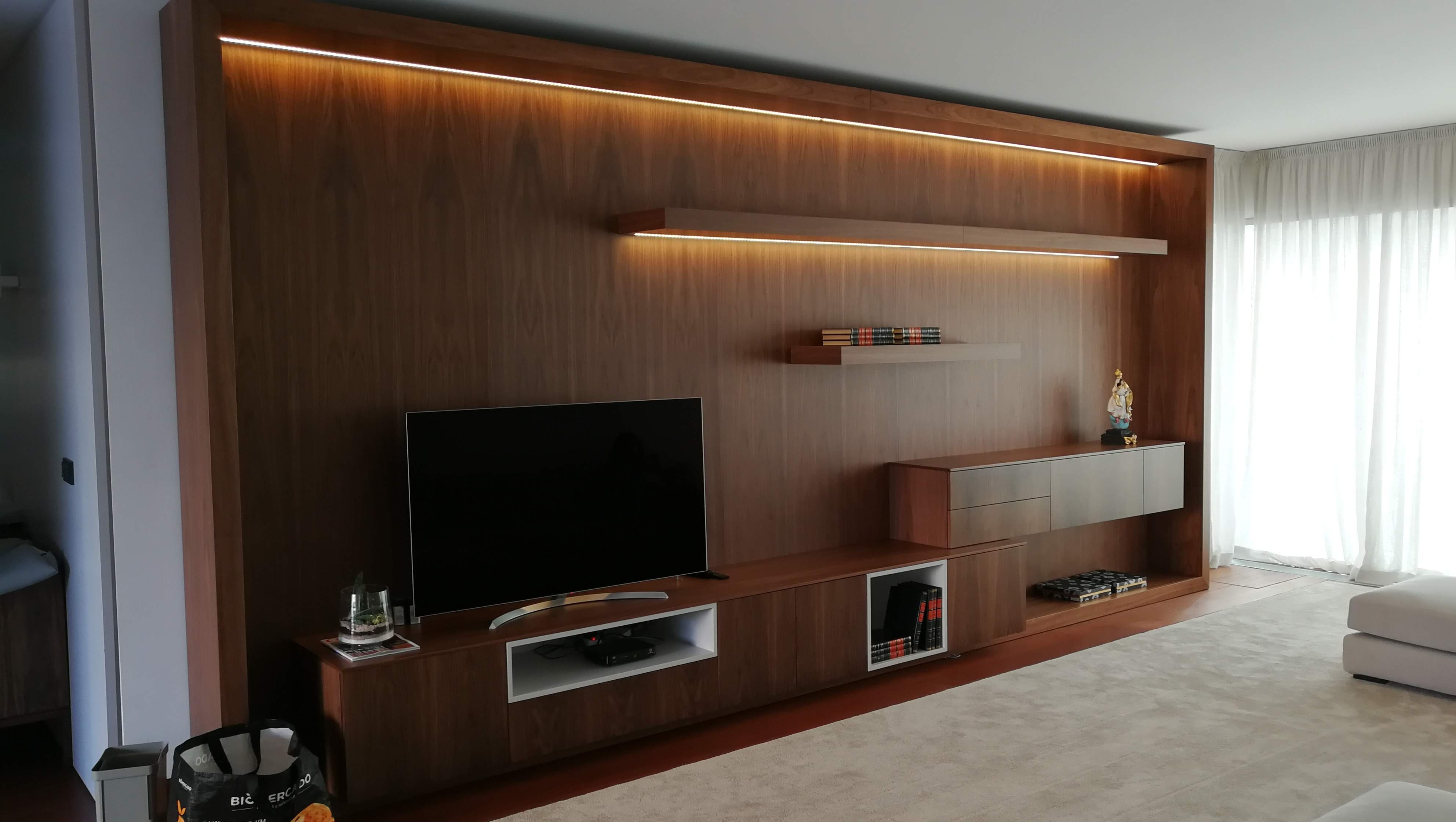 Parede da sala revestida em nogueira com prateleiras flutuantes, movel de TV e iluminacao LED