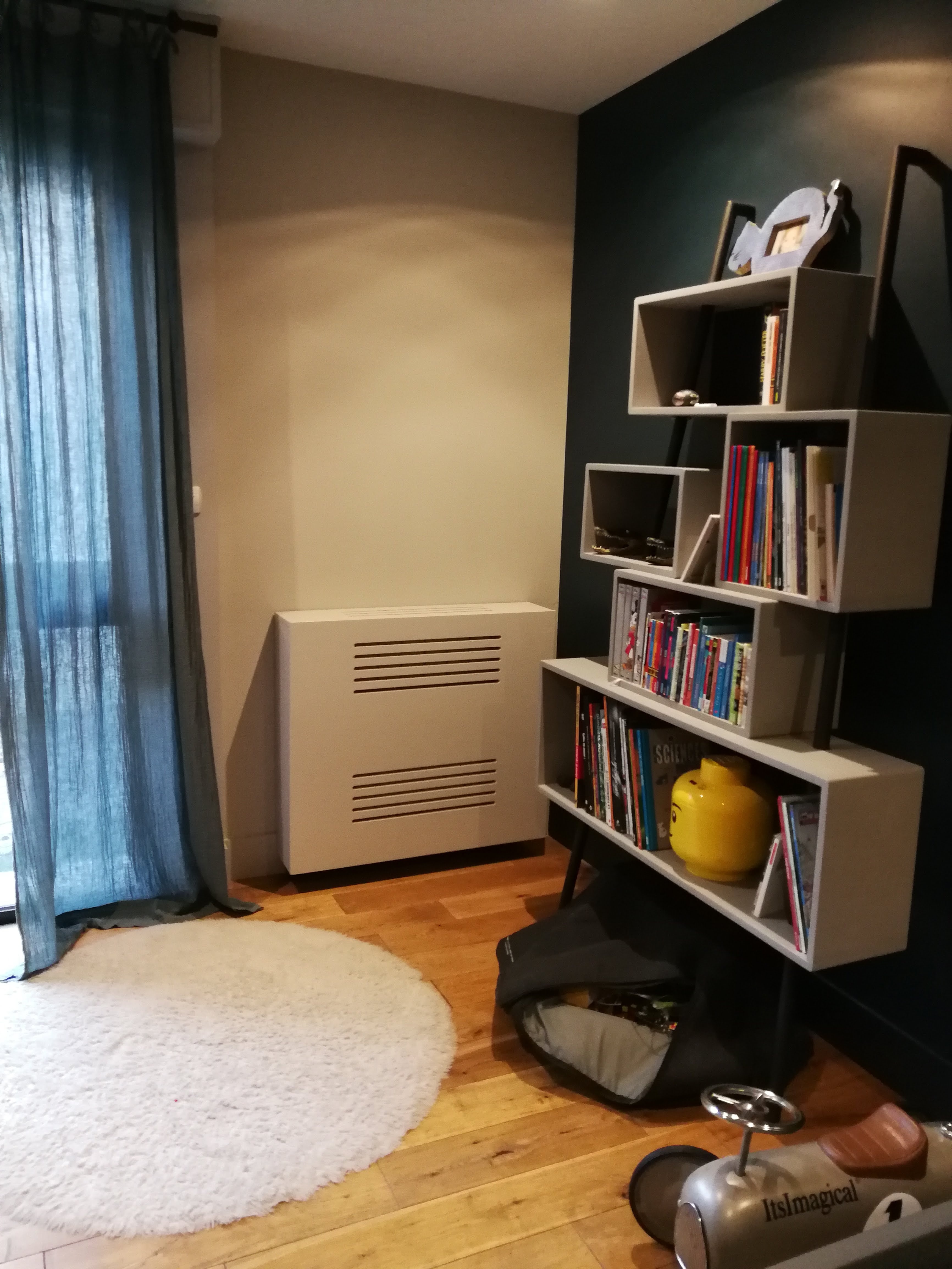 Quarto infantil com parede azul petroleo, estante escalonada branca com livros e tapete redondo