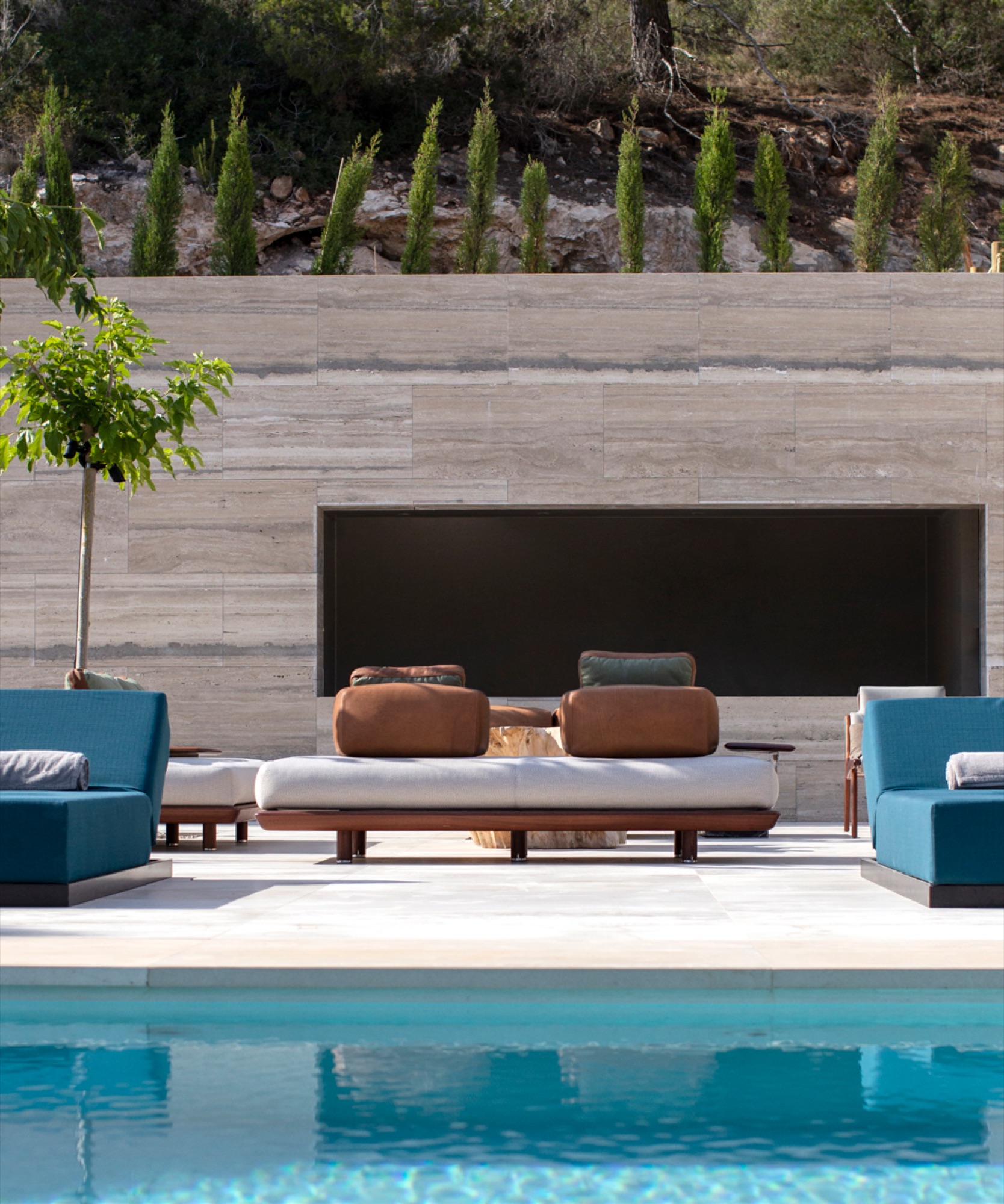Lounge exterior com sofas de design junto a piscina, muro em pedra natural e vegetacao mediterranica