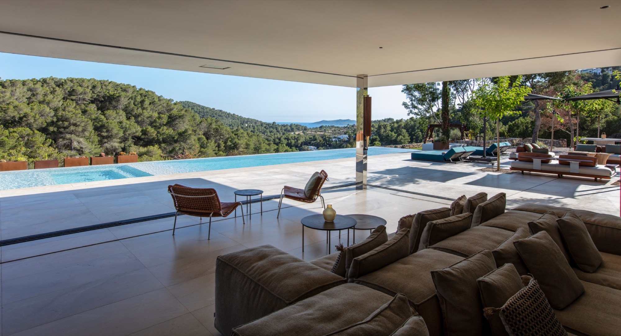 Sala de estar com sofa modular, poltronas de design e abertura total para o terraco e piscina