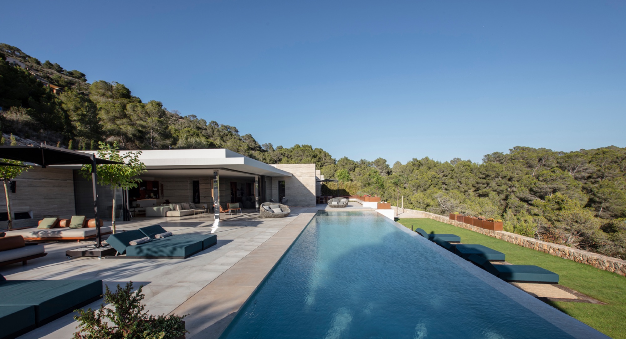 Vista panoramica da villa com piscina infinita, daybed e zona lounge enquadrada pela natureza