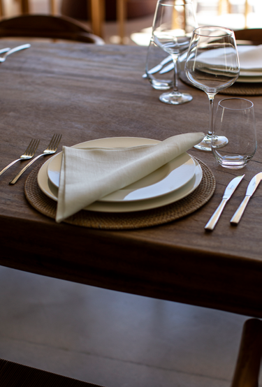 Detalhe de mesa de refeicoes em madeira com lugar individual, guardanapo em linho e copos de cristal