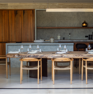 Cozinha exterior com ilha em pedra, armarios em madeira e mesa de refeicoes com cadeiras de design