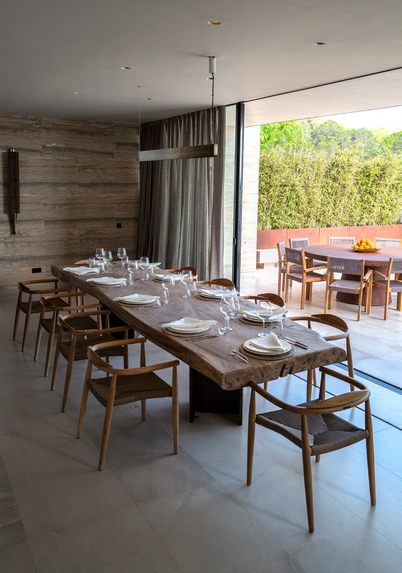 Sala de jantar com mesa em madeira macica, cadeiras Wishbone e abertura para o terraco exterior
