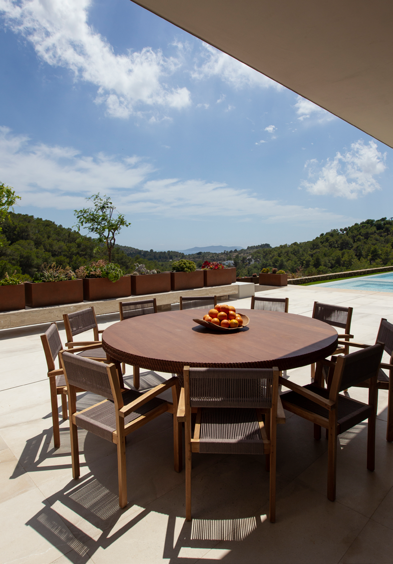 Mesa de refeicoes redonda em madeira no terraco coberto com cadeiras de design e vista para a piscina