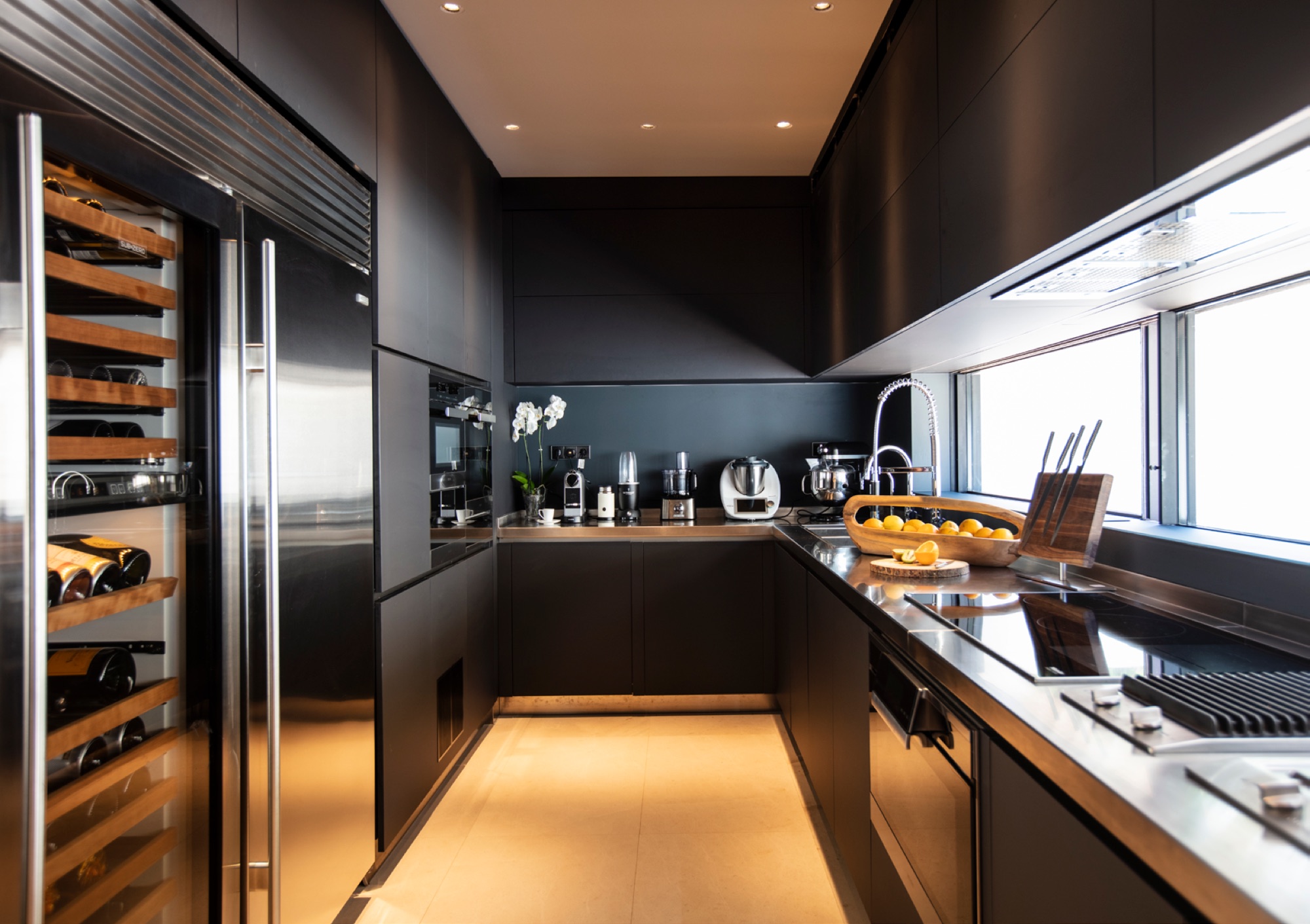 Cozinha profissional em lacado escuro com garrafeira climatizada, iluminacao LED inferior e equipamentos premium