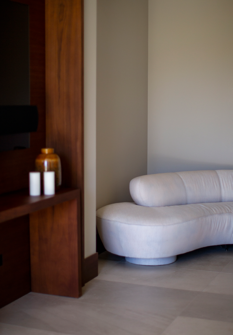 Zona de estar com sofa curvo em tecido claro, nicho com prateleiras em madeira e frascos decorativos