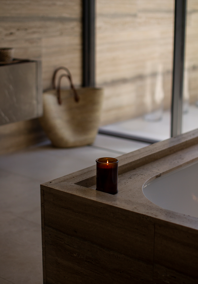 Detalhe da banheira encastrada com rebordo em pedra natural, vela aromatica e cesto artesanal
