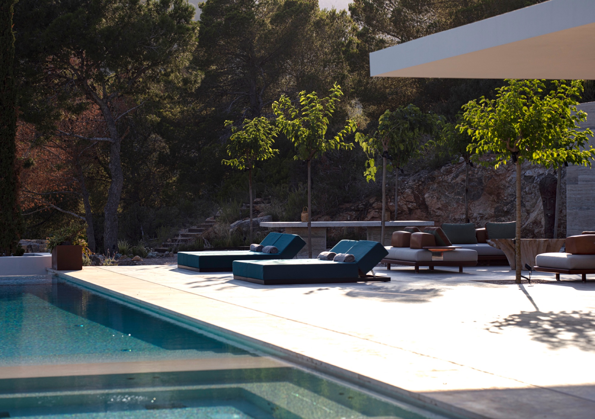 Zona de piscina ao entardecer com espreguicadeiras em teca, daybed e vegetacao mediterranica