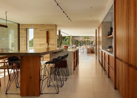 Cozinha em plano aberto com ilha em madeira e pedra, bancos em metal, armarios em nogueira e travertino