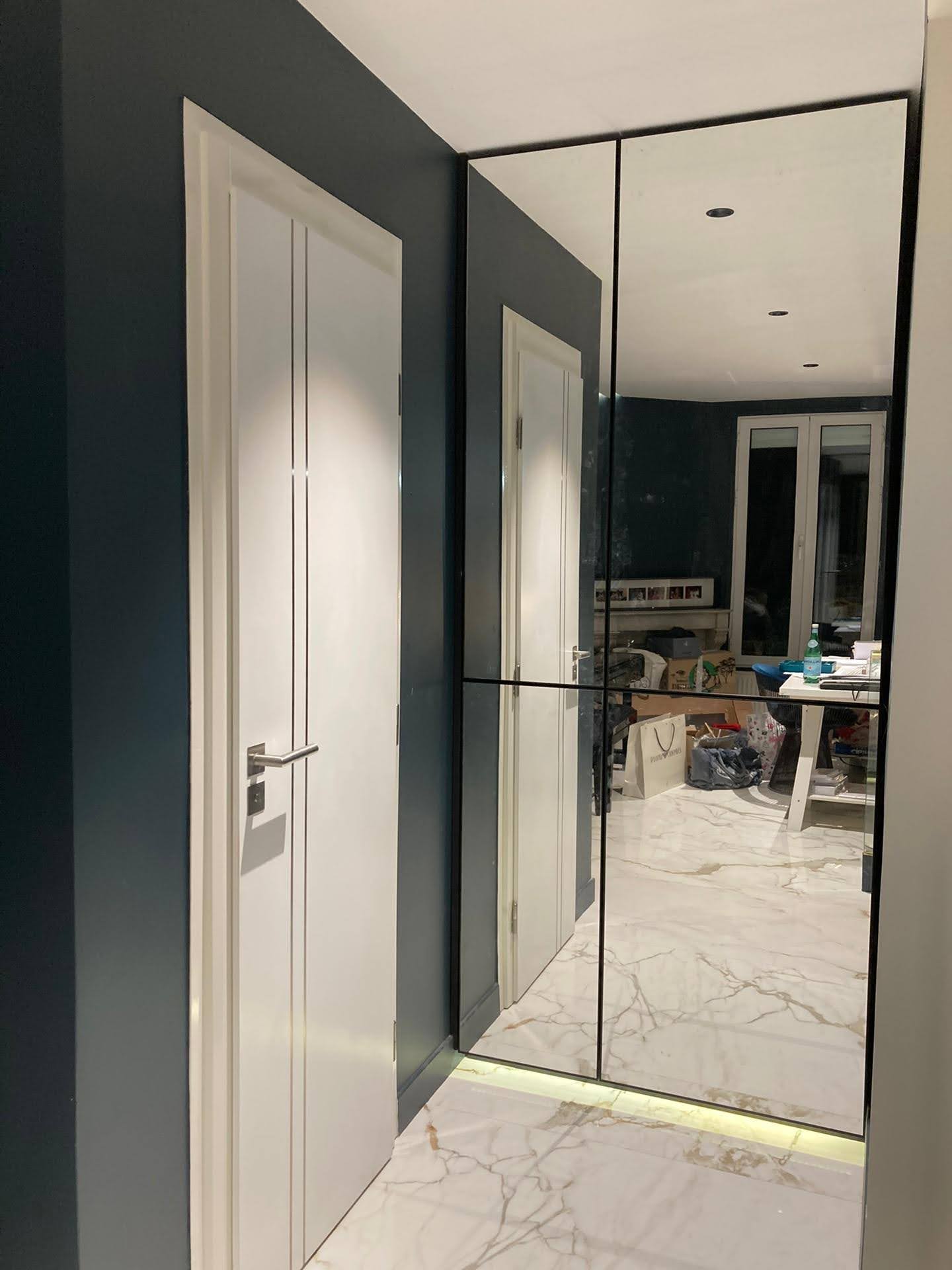 Corredor em azul-escuro com espelho grande de parede e pavimento em porcelanato marmore branco